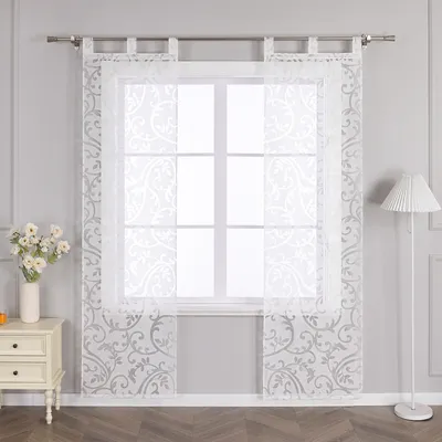 A window with sheer curtains and a bedside table with flowers.