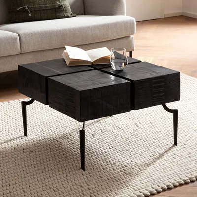 A modern living room scene with a black wooden coffee table in the foreground, a sofa in the background, and a rug underneath the table.