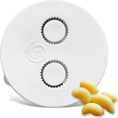 A white pasta maker attachment with two circular cutouts and several shell-shaped pasta pieces in the foreground.
