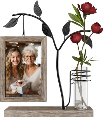 A decorative picture frame with a metal tree branch holding a photo and a glass vase with flowers.