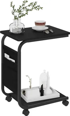 A black C-shaped side table with a plant, a cup and saucer, and sunglasses on top, and a tray with decorative items on the bottom shelf.
