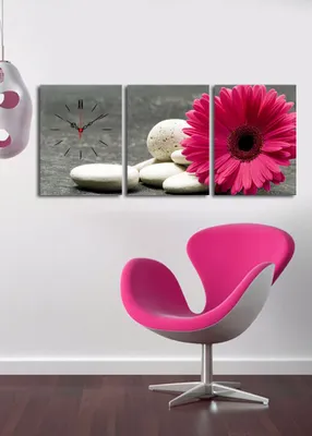 A triptych wall art featuring a clock, stones, and a pink gerbera daisy, displayed above a pink and gray chair.