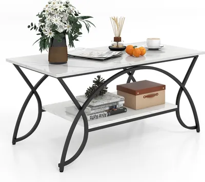 A coffee table with marble-look top and black metal frame, decorated with flowers, books, and oranges.