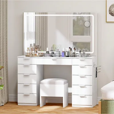 A white vanity table with a large LED mirror, multiple drawers, and a stool, set up in a bedroom.