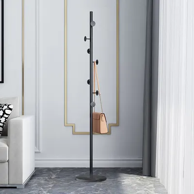 A black coat rack with a tan handbag hanging on it, placed in a room with a white sofa and a decorative wall.