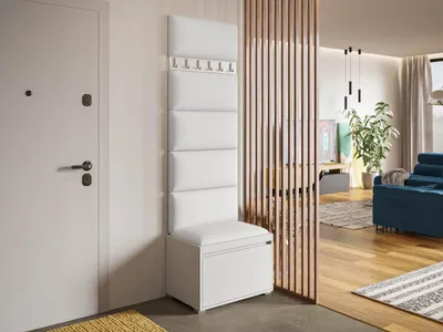 A white entryway storage unit with a bench and coat hooks is shown next to a white door, with a glimpse of a living room through a wooden slat divider.