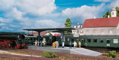 A model train station scene with a steam locomotive and passenger cars.