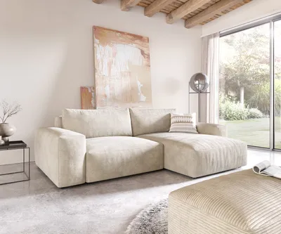 A modern living room with a large sectional sofa, artwork, and a large window overlooking a garden.