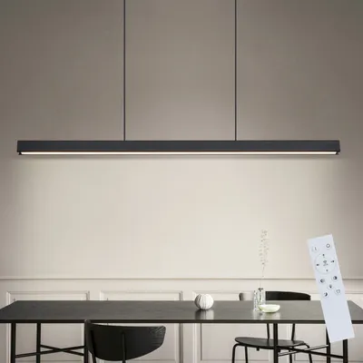 A modern black LED pendant light hangs above a dining table, with a remote control placed on the table.