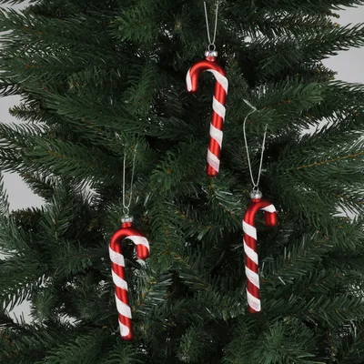Three red and white striped candy cane ornaments hang on a Christmas tree.
