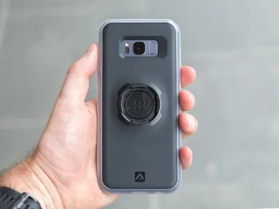 A hand holding a smartphone with a protective case and a mount attached.