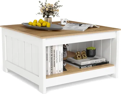 A square wooden coffee table with a white base and a wood-grain top, featuring an open shelf with books and decorative items.