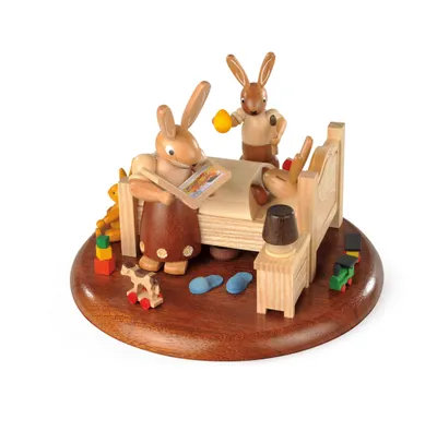 A wooden figurine scene of rabbits in a bedroom setting.