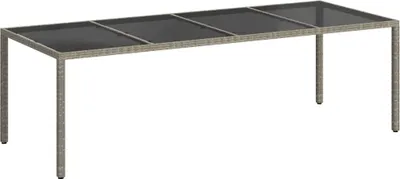 A rectangular outdoor dining table with a grey rattan frame and a dark glass top, shown from a slightly elevated side angle against a white background.