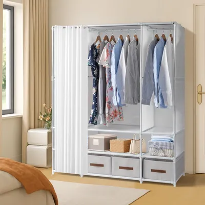 A white fabric wardrobe with clothes hanging on the racks and storage boxes below, placed in a bedroom setting next to a window.