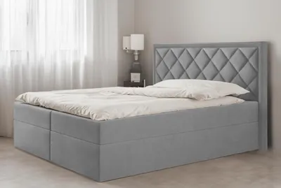 A grey upholstered box spring bed with a diamond-stitched headboard is shown in a bedroom setting.