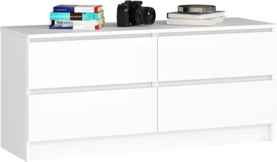 A white dresser with four drawers is shown against a white background. Books and a camera are placed on top of the dresser.