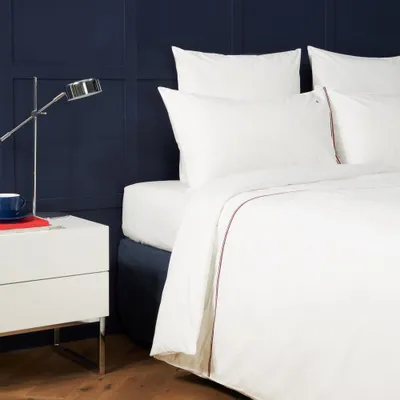 A neatly made bed with white bedding and a dark blue wall.