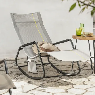 A rocking lounge chair with a hat on it, placed on a stone patio next to a small table with drinks and snacks.
