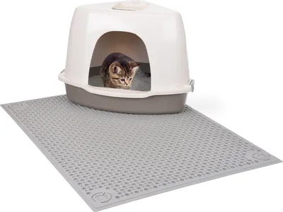 A kitten is inside a covered litter box that is placed on a grey litter mat.