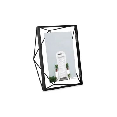 A black geometric picture frame with a picture of a white door and plants inside, set against a white background.