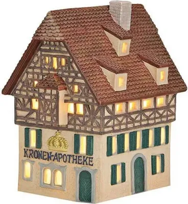 A decorative, illuminated ceramic house with a half-timbered facade and a tiled roof, representing a pharmacy.