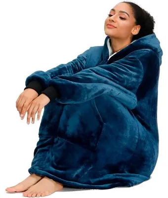 Blaugrüner übergroßer Wearable-Decken-Hoodie mit weißem Sherpa-Futter, getragen von einer Person, die mit angezogenen Knien sitzt