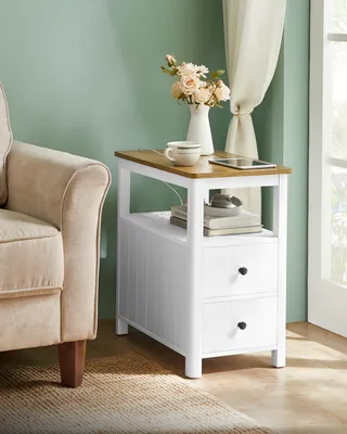 A bedside table with a cup and flowers next to a chair.
