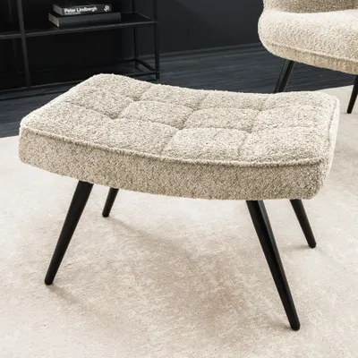 A close-up shot of a bouclé ottoman with black metal legs, placed on a light-colored rug.