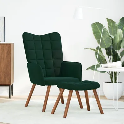 A dark green velvet armchair and ottoman set on a light-colored rug, with a floor lamp and a large potted plant in the background.