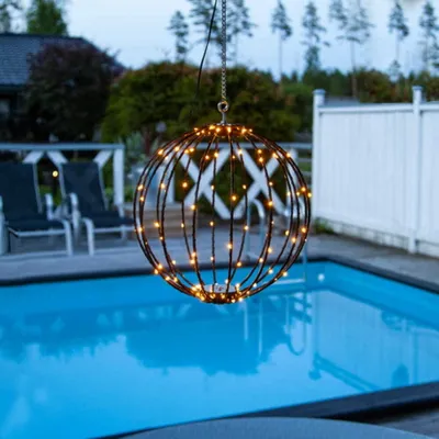 A decorative LED wire ball hangs over a swimming pool at dusk.