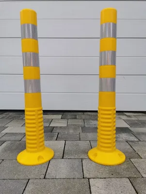 Two yellow traffic posts with reflective silver bands stand on a paved surface in front of a white garage door.