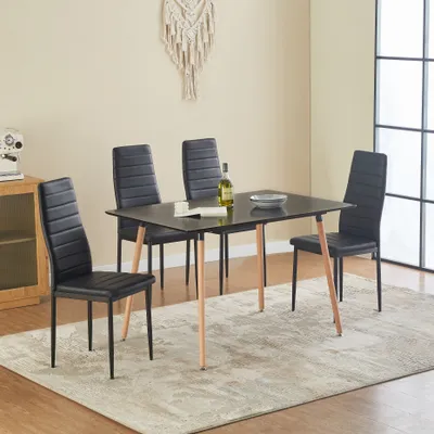 A dining set with a black table and four black chairs with wooden legs, set on a rug in a room.