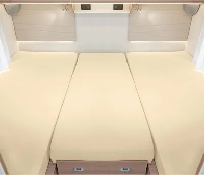 A view of a bed setup in a recreational vehicle or caravan, featuring three mattress sections covered in cream-colored fitted sheets.