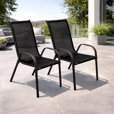 Two black outdoor chairs on a patio with a sofa and plants in the background.