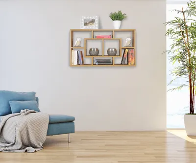 A living room scene with a blue sofa, a wall shelf with books and decor, and a tall plant near a window.