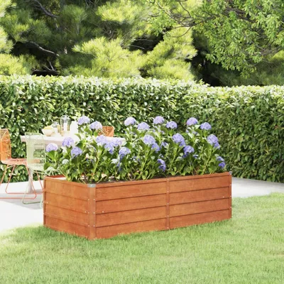 A wooden raised garden bed filled with purple hydrangeas sits on a lawn, with a hedge and trees in the background.