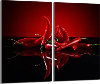 A close-up studio shot of red chili peppers on a reflective black surface with a red background.