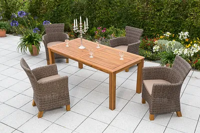 An outdoor patio set with a wooden table and four wicker chairs, surrounded by plants and flowers.