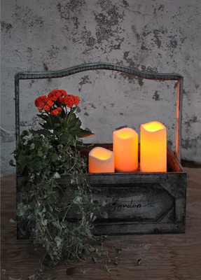 A rustic wooden planter box with a metal frame, containing a plant with red flowers, trailing vines, and three LED candles.