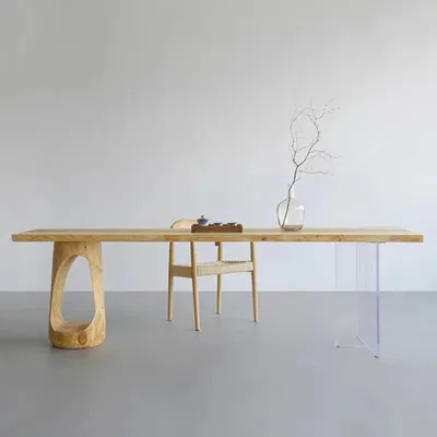 A modern wooden dining table with unique carved legs and clear acrylic legs, set against a plain wall.