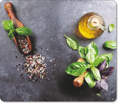 A top-down view of basil leaves, peppercorns, salt, and olive oil on a dark gray surface.