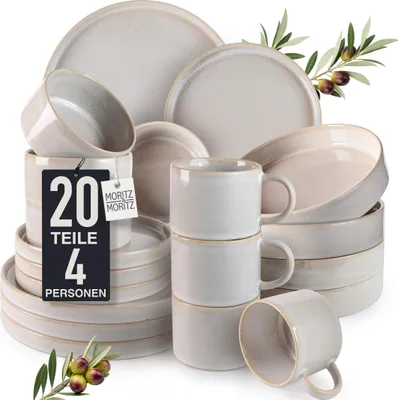 A collection of ceramic dishes and mugs, arranged in stacks and piles, with olive branches and olives in the foreground and upper right.