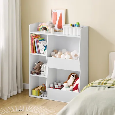 A child's bedroom with a white toy storage shelf filled with books, stuffed animals, and balls, next to a bed with green and white bedding.