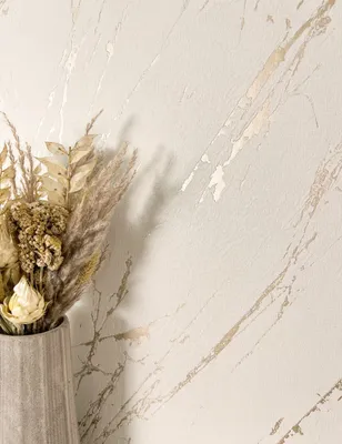 A close-up shot of a vase with dried flowers against a textured wall with a marble-like pattern.