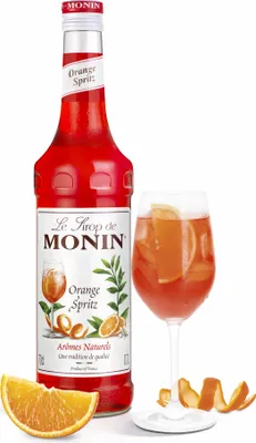 A bottle of Monin Orange Spritz syrup and a glass of the prepared drink, with orange slices and peel.