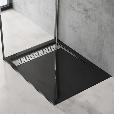 A modern black shower tray with a silver drain, installed in a bathroom with concrete walls and light gray floor.