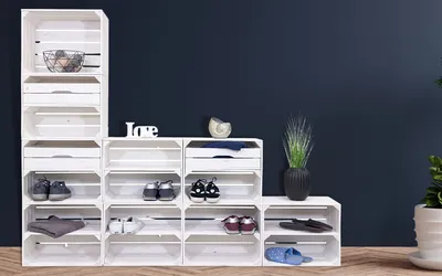 A modular shelving unit made of white wooden crates, arranged in a stepped pattern, displaying shoes and decorative items.