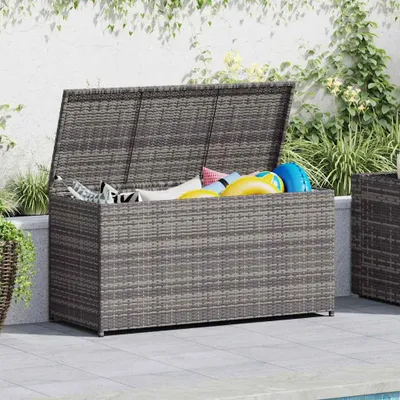 An outdoor storage box filled with pool toys, placed on a patio next to a pool.