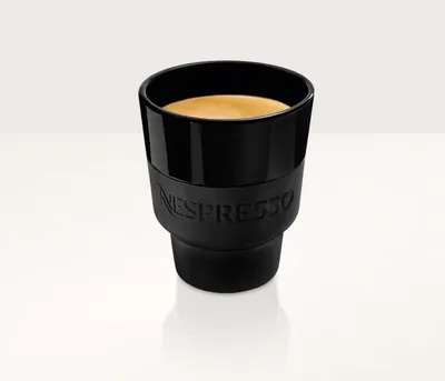 A black Nespresso ceramic cup filled with espresso, shown on a white background with a subtle reflection.